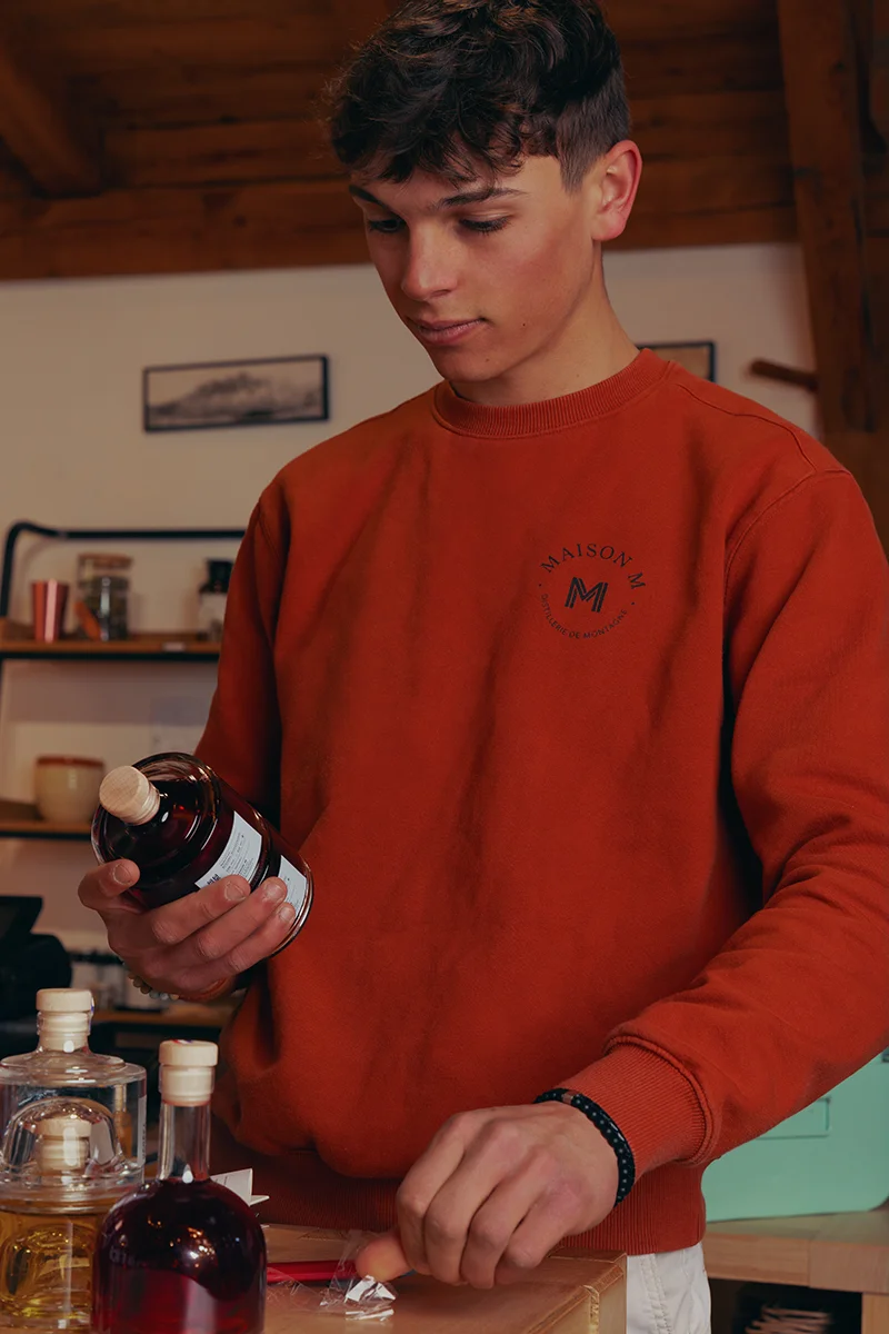 Photo de Jessy Matrat tenant une bouteille de spiritueux à l'intérieur de la distillerie Maison M.