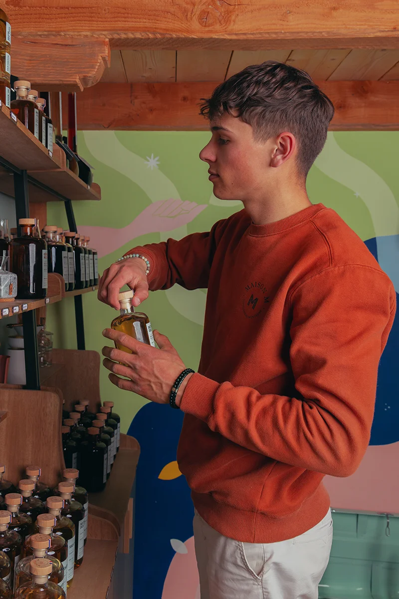 Photo de Jessy Matrat tenant une bouteille de spiritueux à l'intérieur de la distillerie Maison M.